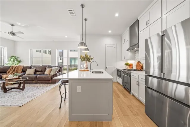 a kitchen with stainless steel appliances a refrigerator a sink dishwasher a stove and white cabinets with wooden floor