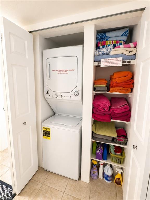 600 Neapolitan Way, Unit 449 Naples, FL 34103 - Photo 21 of 44 Compact laundry closet featuring a white stacked washer and dryer unit, integrated shelving, and light-toned tile flooring