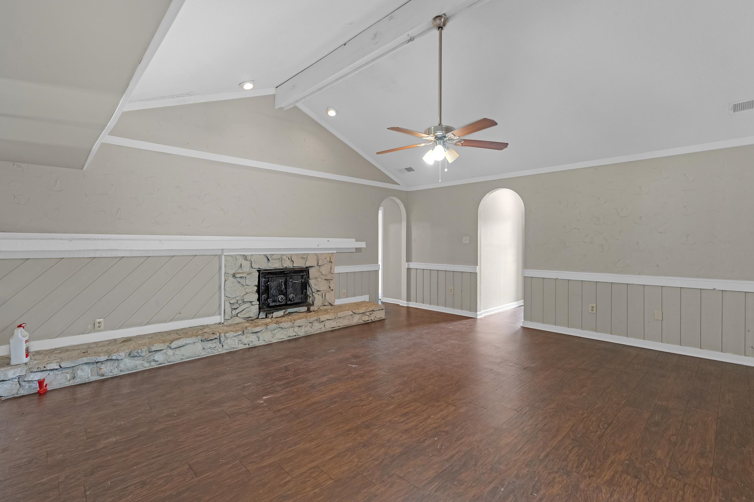 6128 Raintree Drive Memphis, TN 38115 - Photo 5 of 30 Unfurnished living room with dark wood-style flooring, a ceiling fan, a stone fireplace, and a wainscoted wall