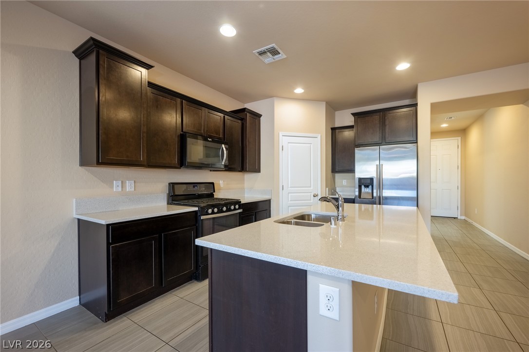 11016 Prairie Grove Road Las Vegas, NV 89179 - Photo 9 of 37 A well-appointed kitchen showcasing an inviting island and dark wood cabinetry with sleek appliances.