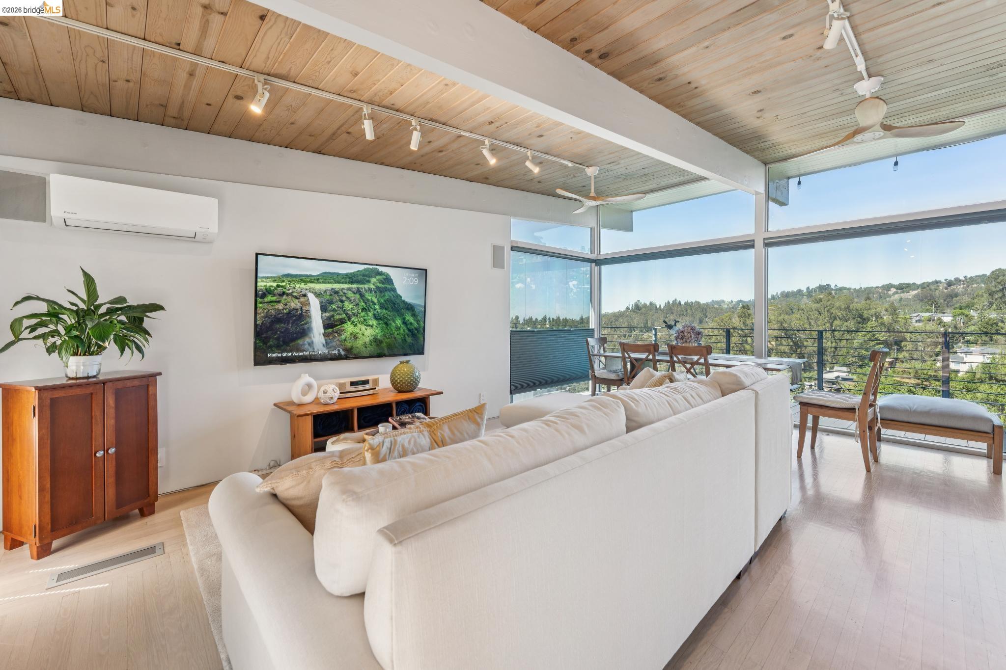 Living room featuring dramatic wood ceiling with exposed beams, two ceiling fans, floor to ceiling windows and included a 65" 4k television