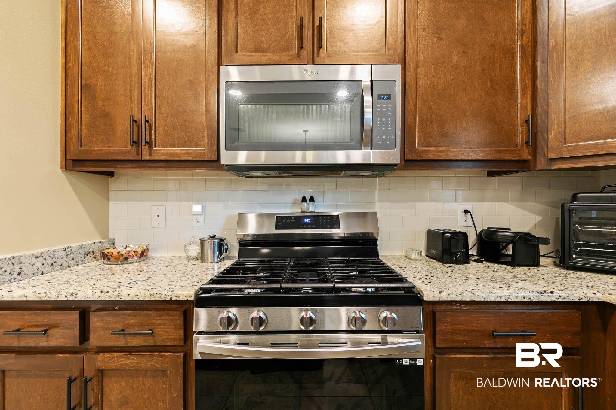 19740 Bunker Loop Fairhope, AL 36532 - Photo 14 of 33 Kitchen with stainless steel appliances, light stone counters, tasteful backsplash, and brown cabinets