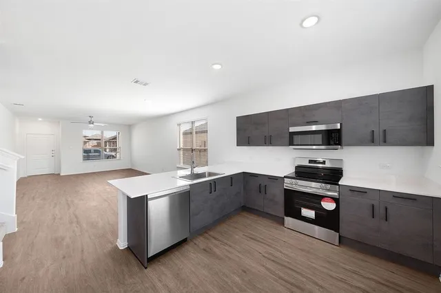 a kitchen with stainless steel appliances a sink wooden floor and black wooden cabinets