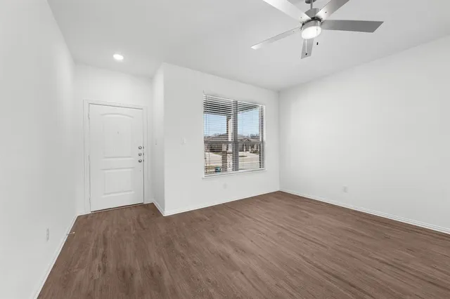 an empty room with wooden floor chandelier fan and windows