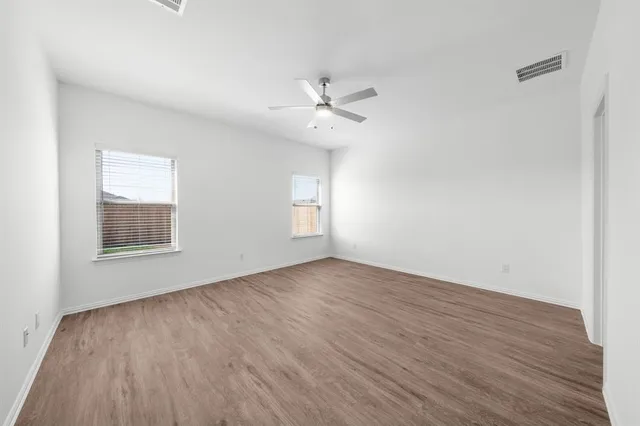 an empty room with wooden floor ceiling fan and windows