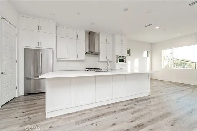 a large kitchen with stainless steel appliances a large counter top a wooden floor and cabinets