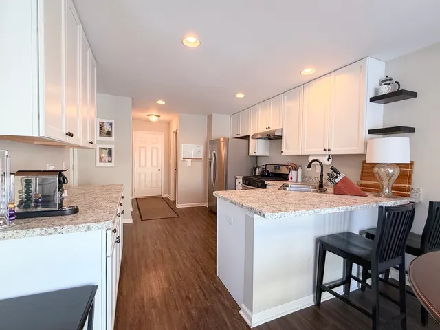 a kitchen with stainless steel appliances granite countertop a refrigerator a stove a sink a dining table and chairs with wooden floor