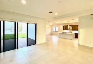 a view of a living room with kitchen view and large windows