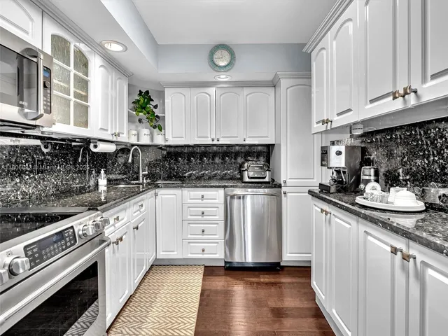 a kitchen with stainless steel appliances granite countertop a stove a sink and white cabinets