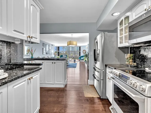 a kitchen with stainless steel appliances kitchen island granite countertop a refrigerator a stove and white cabinets with wooden floor