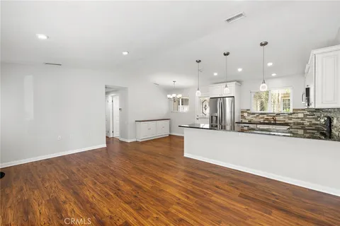 a view of a kitchen with kitchen island a refrigerator wooden floor and a sink