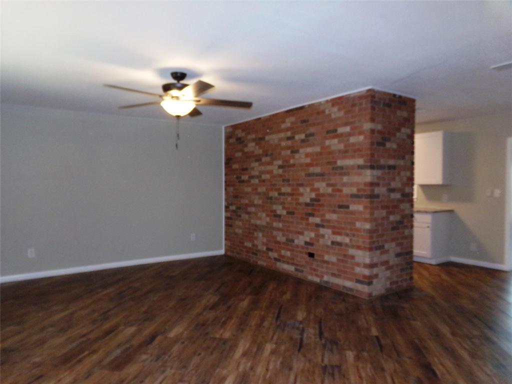 139 Farm To Market 696 Elgin, TX 78621 - Photo 16 of 27 Unfurnished living room featuring dark wood-style floors, brick wall, and ceiling fan