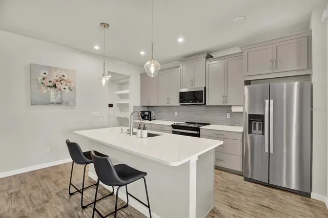 a kitchen with stainless steel appliances a stove a refrigerator a sink and white cabinets with wooden floor