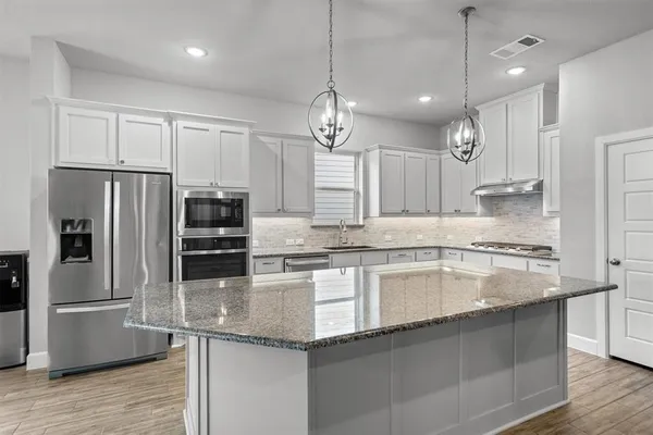 a large kitchen with granite countertop a large counter top a sink stainless steel appliances and cabinets