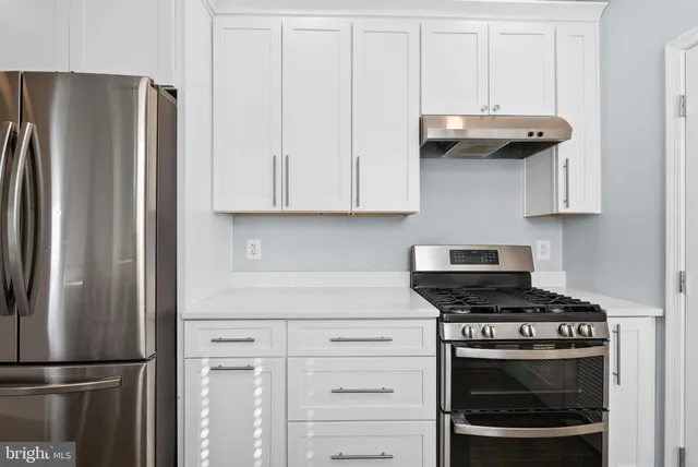 a kitchen with stainless steel appliances a refrigerator a stove and white cabinets with wooden floors