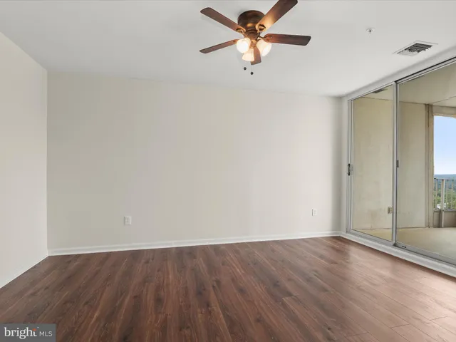 an empty room with wooden floor fan and windows