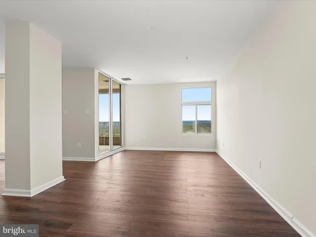 a view of an empty room with wooden floor and windows
