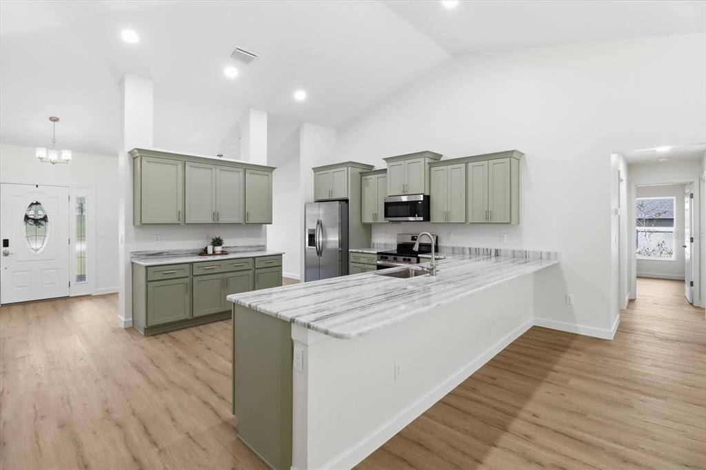 13418 Cormorant Road Weeki Wachee, FL 34614 - Photo 16 of 46 a large kitchen with kitchen island a sink a stove a refrigerator and white cabinets with wooden floor