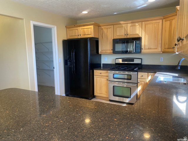 83 Canterbury Circle Logan, UT 84321 - Photo 5 of 23 Kitchen featuring black appliances, dark stone counters, light wood finish cabinets, recessed lighting, and a textured ceiling