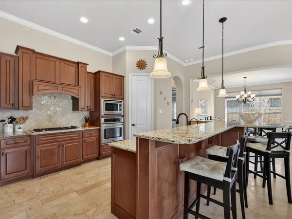 a kitchen with stainless steel appliances kitchen island granite countertop a table chairs sink and wooden cabinets