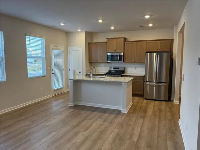 a kitchen with stainless steel appliances granite countertop a refrigerator a sink dishwasher a stove and white countertops with wooden floor