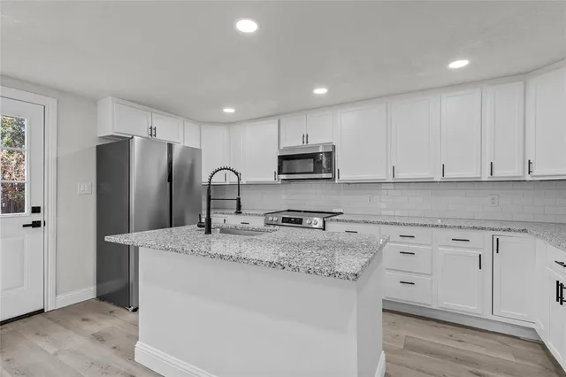 a kitchen with stainless steel appliances granite countertop a refrigerator a sink a stove a microwave and white cabinets with wooden floor