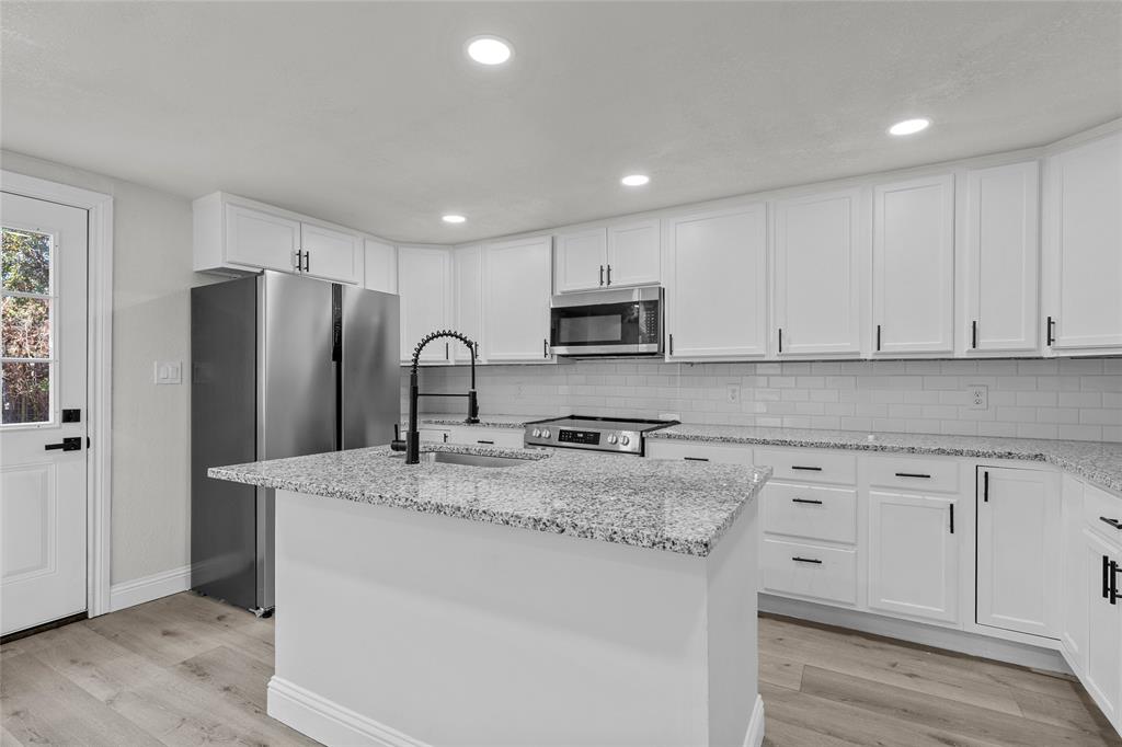 3530 Bluebird Street Bellmead, TX 76705 - Photo 3 of 24 a kitchen with stainless steel appliances granite countertop a refrigerator a sink a stove a microwave and white cabinets with wooden floor