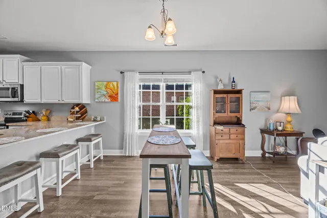 a kitchen with stainless steel appliances granite countertop a stove top oven a refrigerator a dining table and chairs with wooden floor