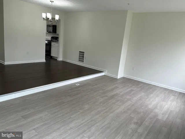 an empty room with wooden floor and kitchen view