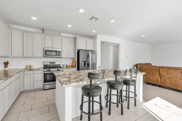 a kitchen with stainless steel appliances granite countertop a stove top oven a sink a dining table and chairs