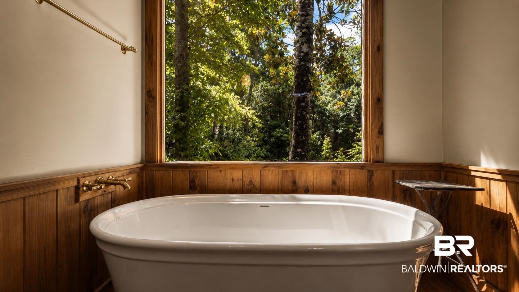14587 Ridge Road Summerdale, AL 36580 - Photo 23 of 44 Freestanding soaking tub with a wall-mounted brass faucet, set against a backdrop of natural wood paneling and a large window overlooking mature trees