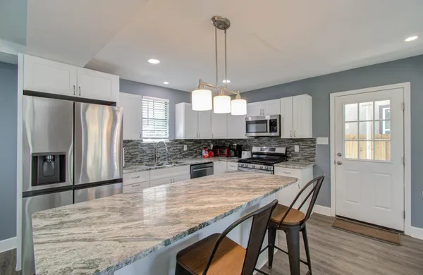 a kitchen with stainless steel appliances granite countertop a refrigerator a sink dishwasher a stove and white cabinets with wooden floor