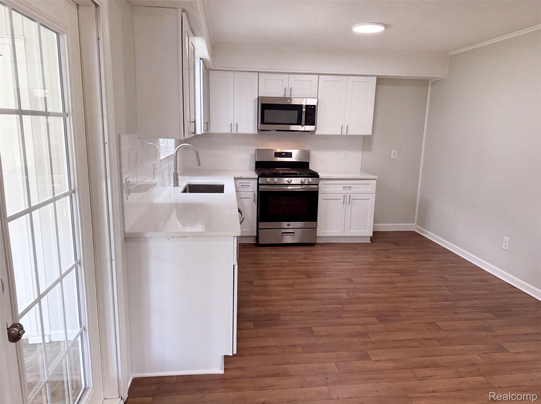 3211 24 Mile Road Utica, MI 48316 - Photo 6 of 18 Updated kitchen featuring white cabinetry, stainless steel gas range and microwave, white refrigerator with ice and water dispenser, wood-finish flooring throughout, and recessed ceiling lighting