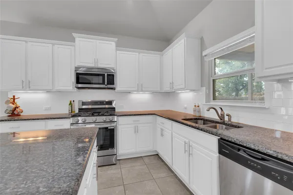 a kitchen with granite countertop a sink a stove top oven and cabinets
