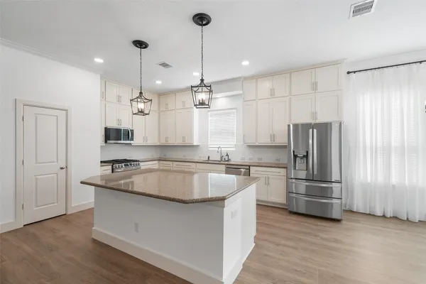 a kitchen with stainless steel appliances granite countertop a refrigerator a sink dishwasher a oven and white cabinets with wooden floor