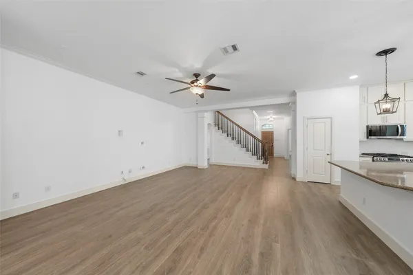 an empty room with wooden floor ceiling fan and kitchen view