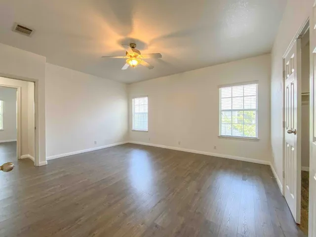 an empty room with wooden floor fan and windows