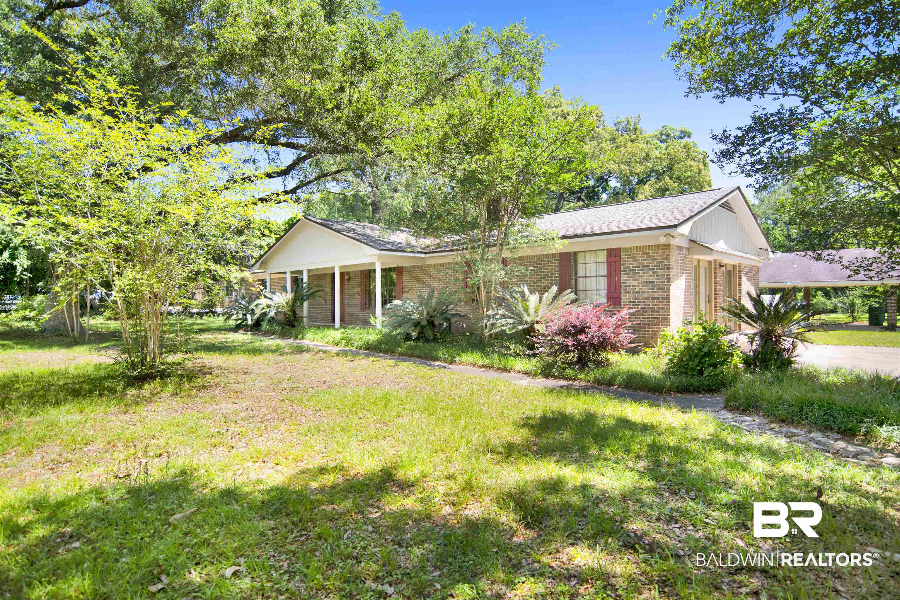 30888 Cemetery Road Daphne, AL 36527 - Photo 33 of 36 Brick exterior with a covered front porch featuring white columns, a shingled roof, a paved driveway, and mature landscaping