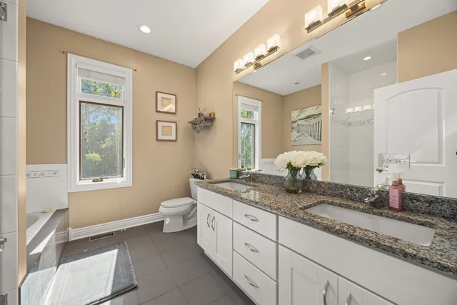 a spacious bathroom with a granite countertop double vanity sink a mirror and a toilet