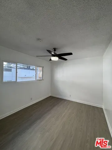 a view of an empty room with wooden floor and a ceiling fan