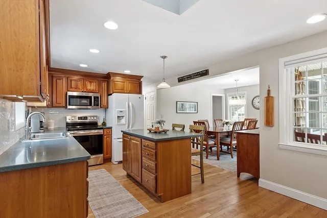 a kitchen with stainless steel appliances granite countertop a stove top oven a sink dishwasher a dining table and chairs with wooden floor