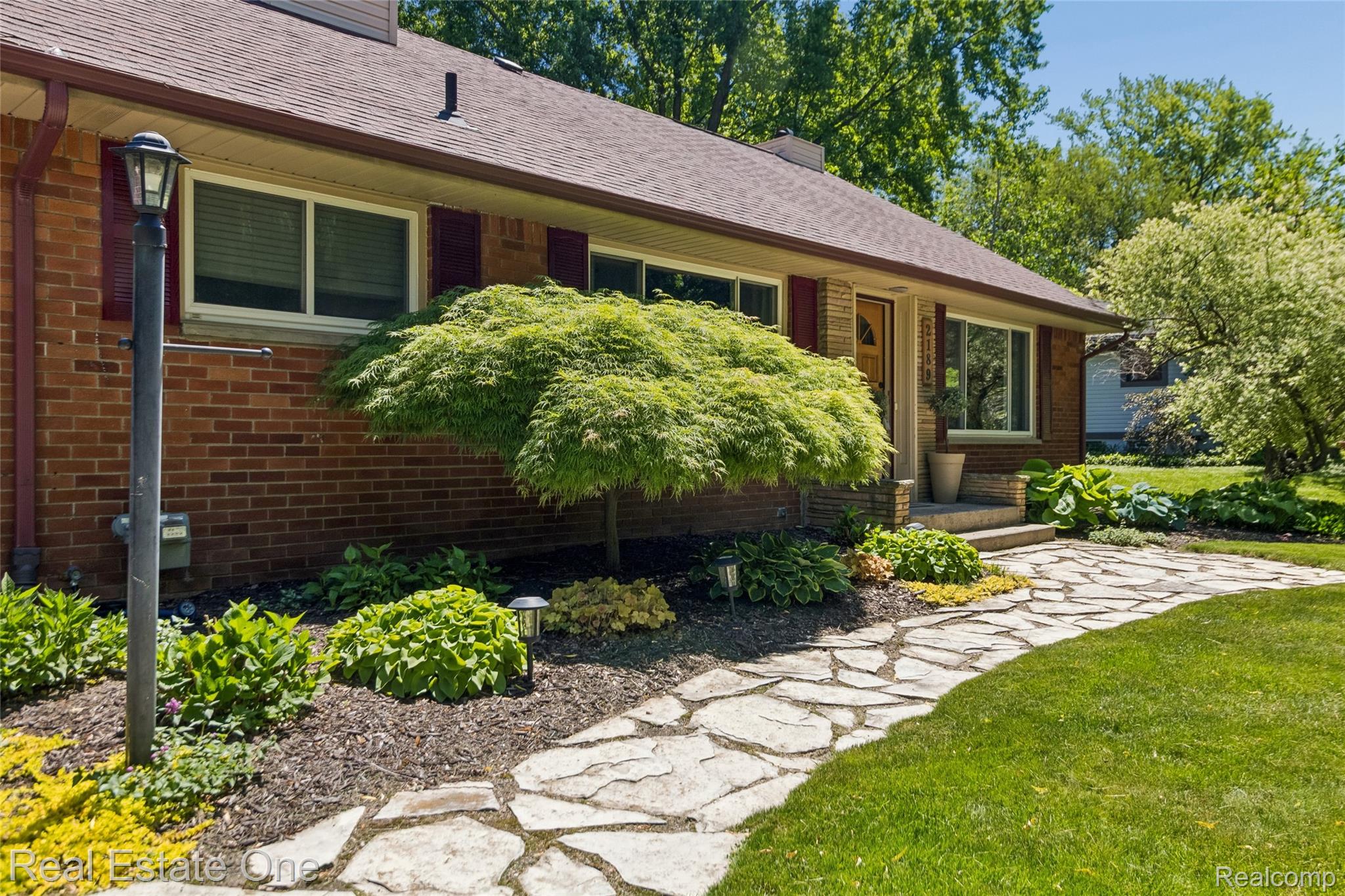 2189 Devonshire Road Bloomfield Hills, MI 48302 - Photo 46 of 50 Brick exterior featuring white-trimmed windows with red shutters, a flagstone walkway, and mature landscaping
