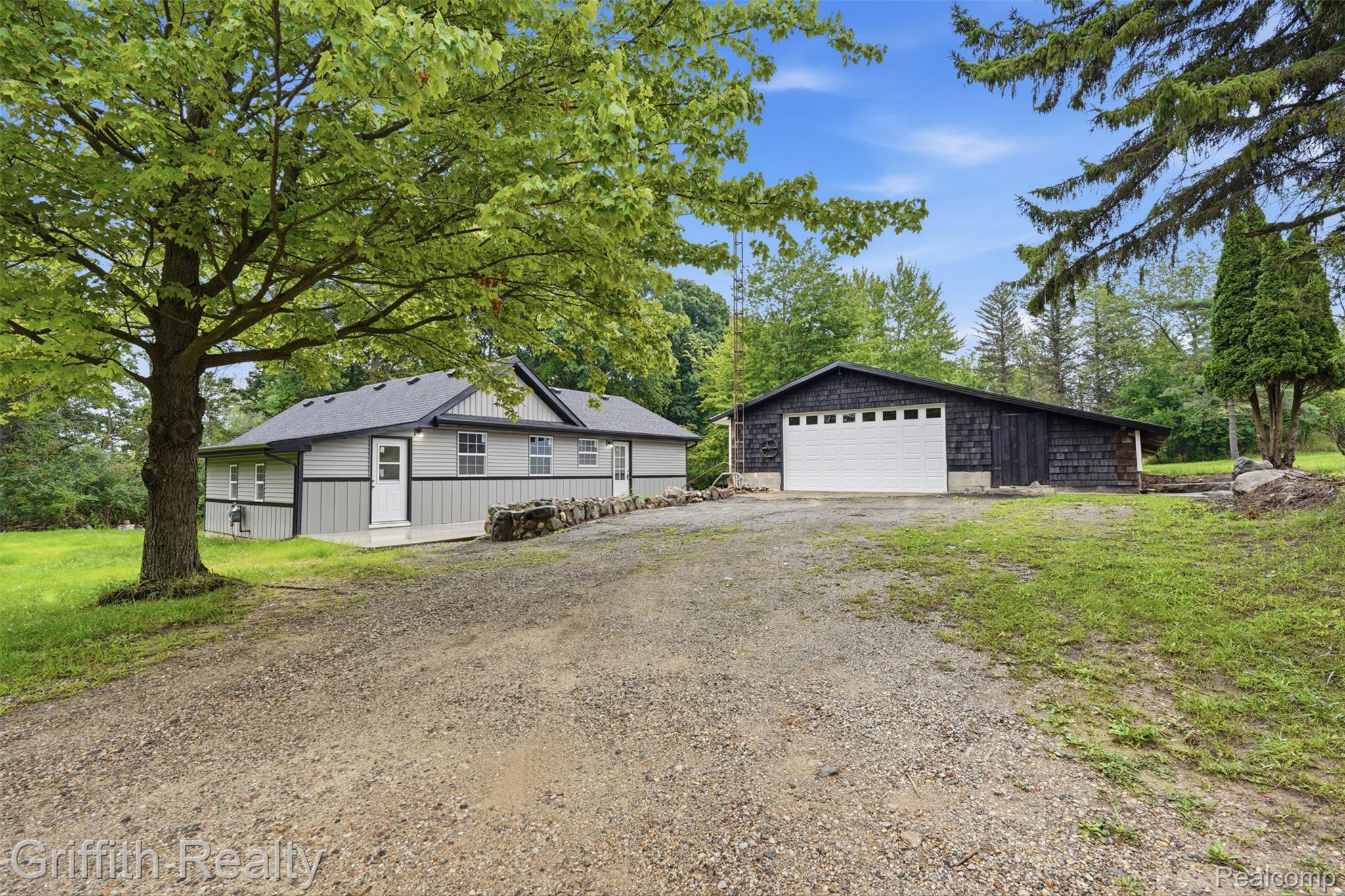 5820 Mack Road Howell, MI 48855 - Photo 2 of 60 Gravel driveway leading to a residence with light gray siding and a detached dark-clad garage with a white sectional door