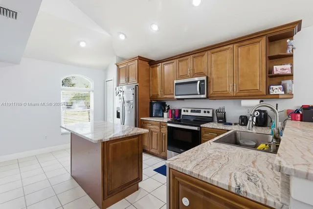 a kitchen with stainless steel appliances granite countertop a stove top oven a sink dishwasher and a refrigerator with wooden cabinets