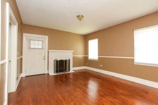 an empty room with wooden floor fireplace and windows