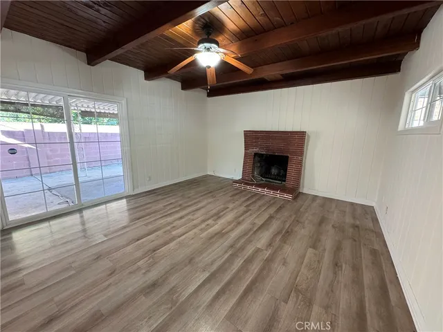 a view of an empty room with wooden floor fireplace and a window