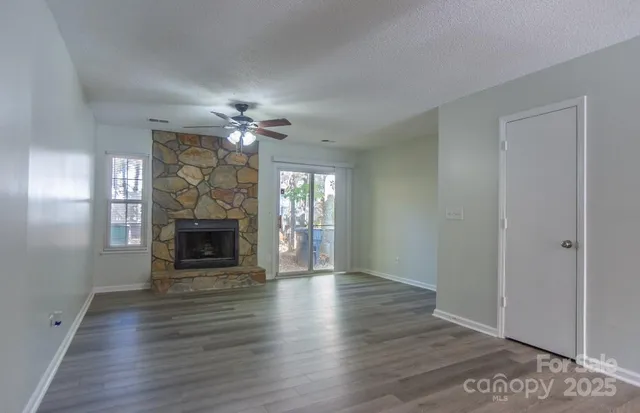 an empty room with wooden floor a fireplace a ceiling fan and windows
