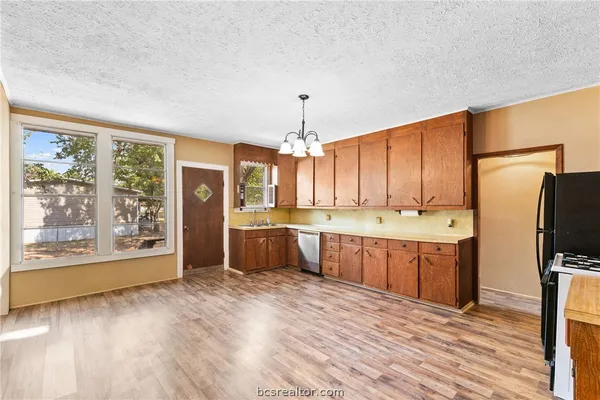 a kitchen with stainless steel appliances granite countertop a refrigerator a sink dishwasher a stove and a dining table with wooden floor