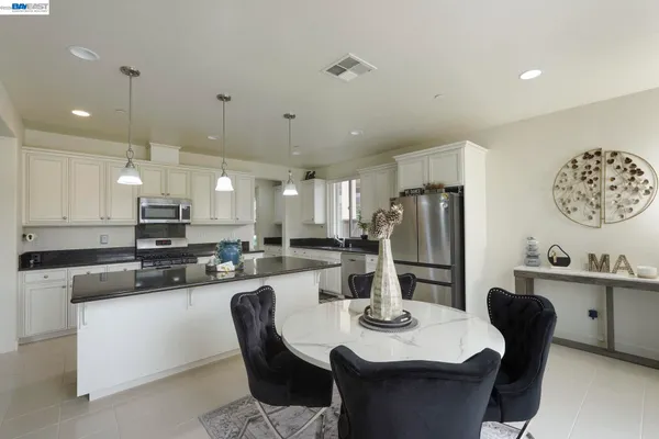 a kitchen with stainless steel appliances kitchen island granite countertop a dining table chairs and a refrigerator