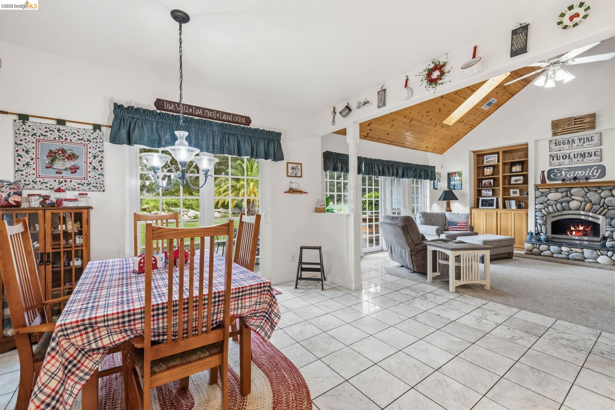 18450 Lambert Lake Road Sonora, CA 95370 - Photo 32 of 87 Open concept living space featuring white tile flooring, a vaulted wood-paneled ceiling, and a river rock fireplace with built-in cabinetry